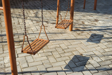 Durable orange iron swings set on a sunny playground with paving block floor. Features industrial metal chains and minimalist design for outdoor park equipment.