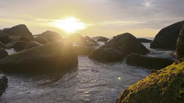 Rocks and rippling water among stones on sea coast while parasail flies high in sky at sunset. Active rest and extreme amusement at ocean exotic resort. Seascape nature