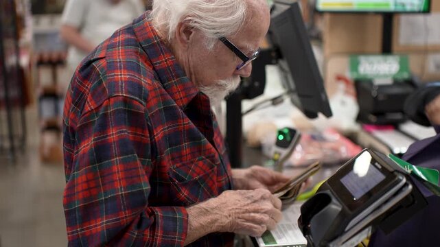Elderly man checks out groceries at a self checkout station in a grocery store while buying fresh produce and other items.