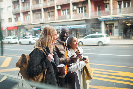 Three friends with coffee and shopping bags walking on city street