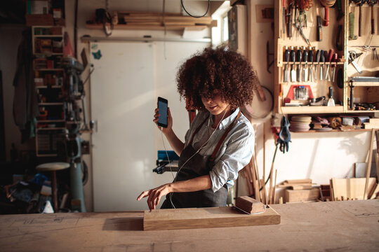 Craftsperson measuring wood while using smartphone in carpentry workshop