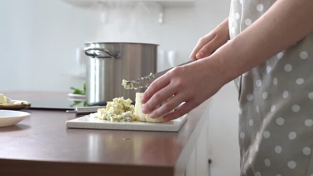 woman slices blue goat cheese in the kitchen, girl crumbles cheese on cutting board at home