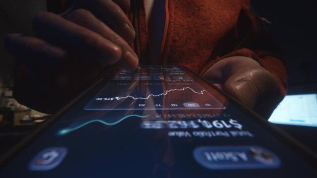 Close-up male hand holding smartphone with financial investment app showing portfolio growth and rising chart. Evening indoor low light scene with stock market data, fintech wealth management at home
