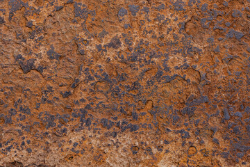 Weathered rusty surface captures rough textures in a natural environment. Daytime light enhances the rugged appearance, creating a striking visual of decay and time.