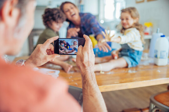 Parent photographing playful children baking at home