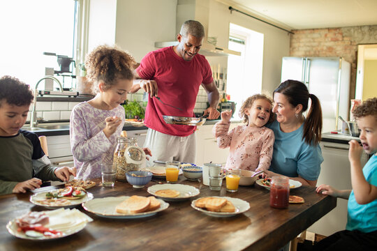 Parents and children eating breakfast together in home kitchen