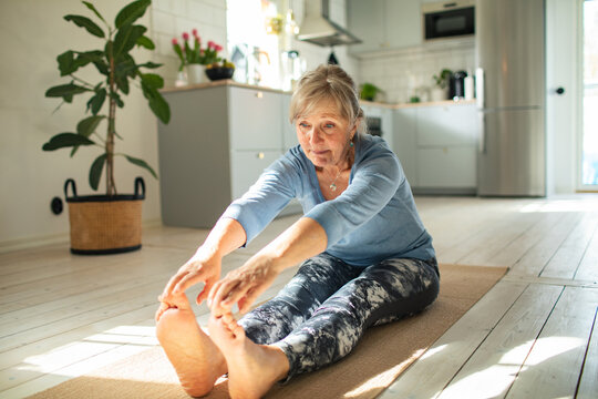Senior woman stretching on yoga mat in home kitchen