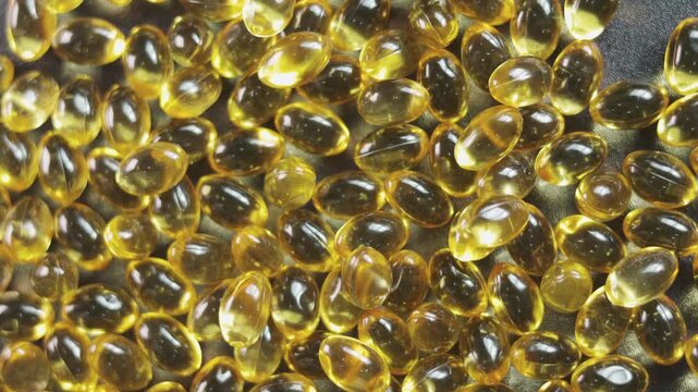 Top-down, close-up video of golden softgel capsules, like vitamin or fish oil supplements, slowly rotating on a turntable on black background showing concepts of healthcare, medicine, and nutrition.