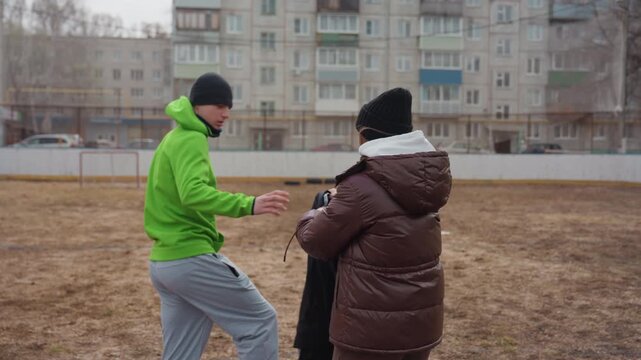 white coach helps player adjust jacket on suburban field, supportive handoff and brief pep talk, residential courtyard backdrop, breath visible in cold air, preparation for training