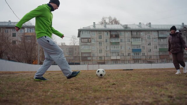 courtyard match showing white men facing off over ball on patchy grass, friendly competitive energy, quick passes and toe taps, apartment facades and fence frame scene, communal sport moment