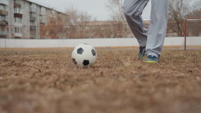 player approaching ball ready to strike, white teen paces forward on worn pitch with goalkeeper behind, measured foot contact and casual green top signal focused warmup before decisive shot