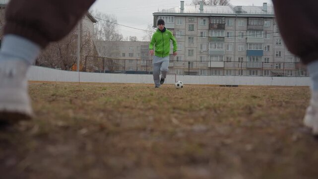athlete moves swiftly across uneven field, individual soccer player charges forward on rugged residential surface, determined footballer advances towards net across patchy urban playing field