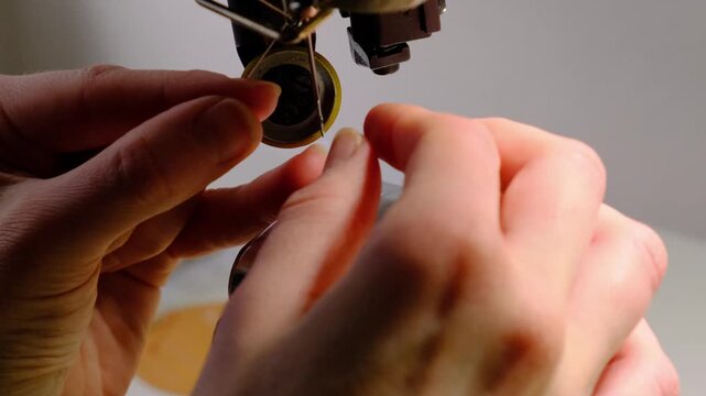 Close-up of hands threading a needle on an industrial sewing machine in a leather workshop. Precise manual preparation before sewing leather goods.