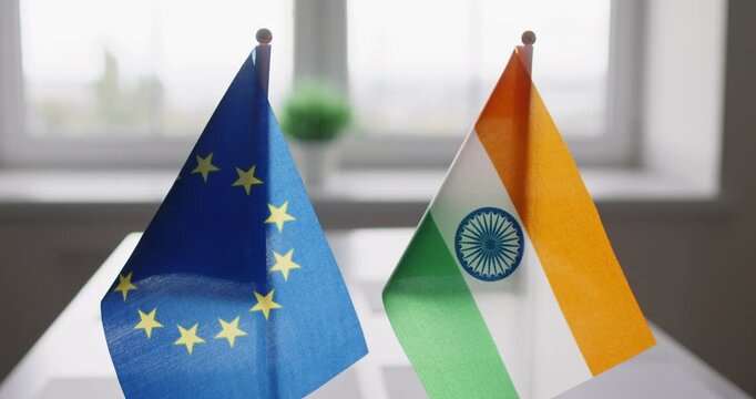 Flags signal diplomacy and negotiation between EU, India. Two desktop flags on a conference table, indicating formal meeting dialogue. Symbolizes bilateral diplomatic trade negotiations.