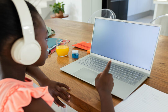 Silver laptop sitting on wooden dining table with headphones, open notebook, orange juice
