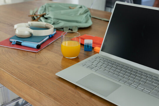 Silver laptop sitting on right of table green backpack with headphones and notebooks, copy space