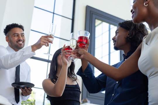 Red wine and champagne glasses are clinking near black-framed windows in bright event space