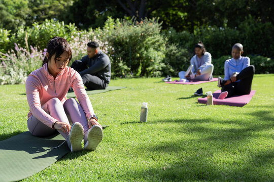 Green and pink yoga mats are lying on sunlit park lawn with water bottles nearby