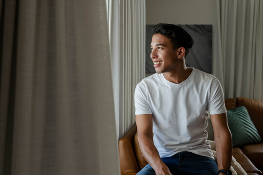 Adult African American man sitting in living room on brown couch, wearing white T-shirt and watch