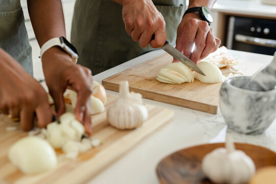 Onion is being thinly sliced on wooden cutting board on light countertop in home kitchen