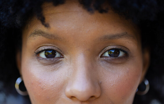 Adult African woman holding steady gaze, focusing on eyes against dark blur with hoop earrings