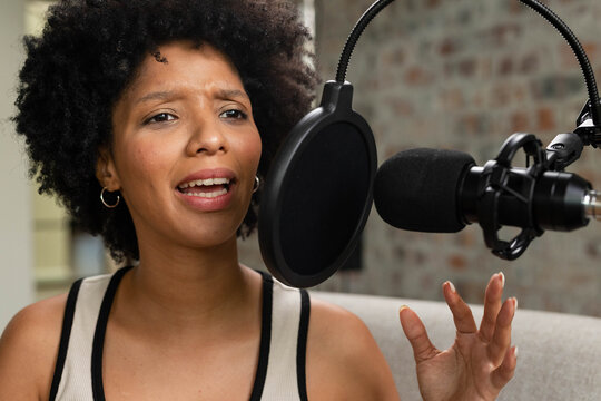 African American woman wearing sleeveless beige top speaking into mic with pop filter in studio