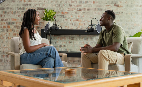 African co-hosts sitting in studio lounge recording conversation with microphones and glass table