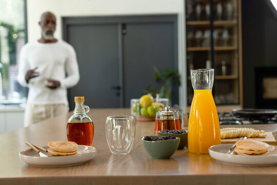 Breakfast spread is sitting on wooden kitchen island, with pancakes, syrup, juice, berries