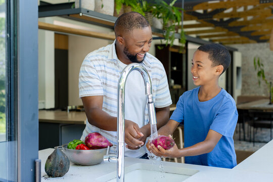 African father and son washing purple tuber under chrome faucet at kitchen sink, colander visible