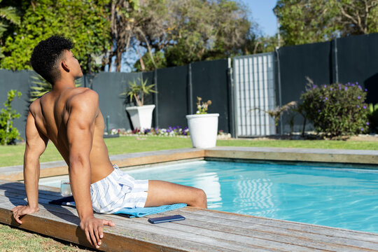 African American man sitting on pool deck wearing shorts beside smartphone glass, copy space