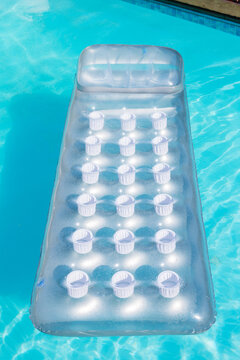Transparent pool lounger is floating on turquoise water with raised headrest, cup wells, pool tile