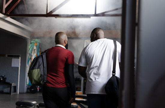 African men walking toward weights in industrial gym in sportswear, carrying backpack and gym bag