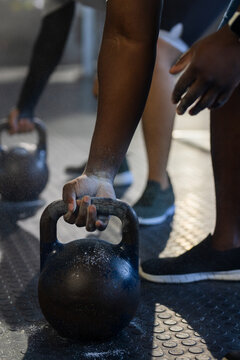 African American men gripping kettlebells, training at gym on rubber floor with chalk dust