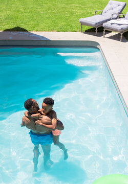African American father and son splashing in shallow yard pool with green float and chaise lounges
