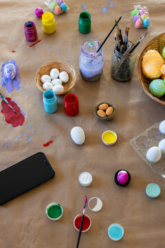 Paint pots and brushes are sitting on brown kraft paper table, surrounding single white egg