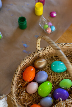 Wicker basket is sitting on kraft paper at craft table, holding colorful plastic eggs