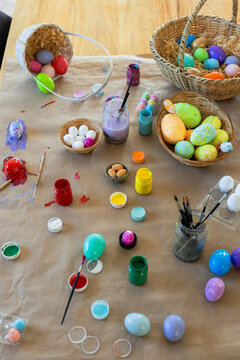Painted and unpainted eggs are drying and spilling on wooden craft table, paint jars and brushes