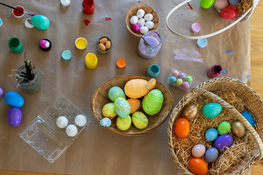 Wicker baskets holding colorful painted eggs are sitting on kraft paper table, with paint jars