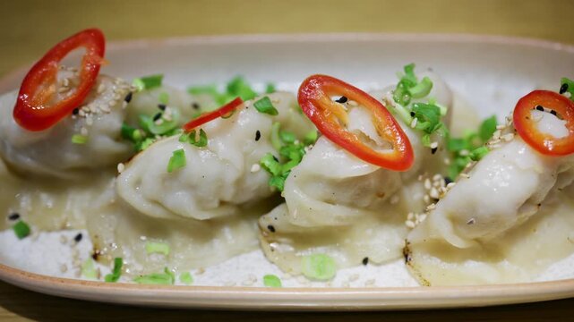 Row of pan fried dumplings topped with sliced red chili and green onions on a ceramic plate