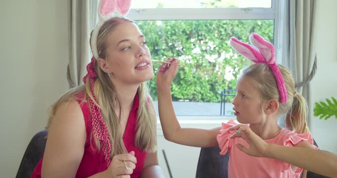 Mother and daughter painting faces at table, child painting nose leading mother drawing whiskers
