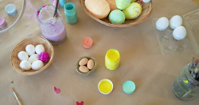 Camera is panning down and right, revealing paint pots, brushes, and pastel eggs to showcase setup