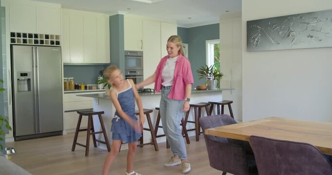 Mother and daughter dancing playfully after child leading, mirroring by kitchen island