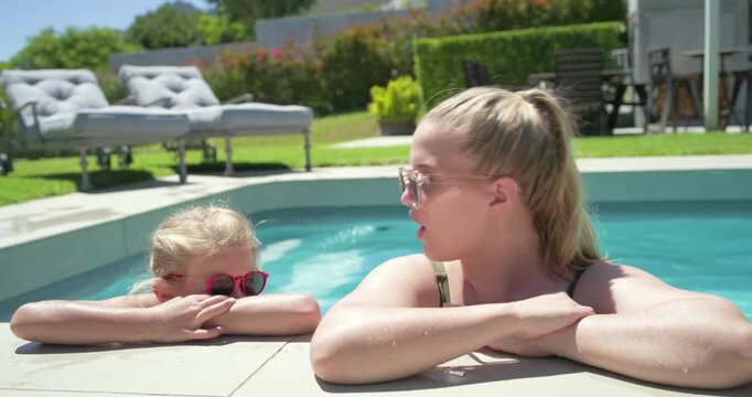 Mom and daughter leaning on home pool edge pointing daughter climbing posing to cam pink shades