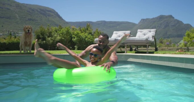 Father and son in home pool, father entering, reaching, spinning green float, playing son in shades