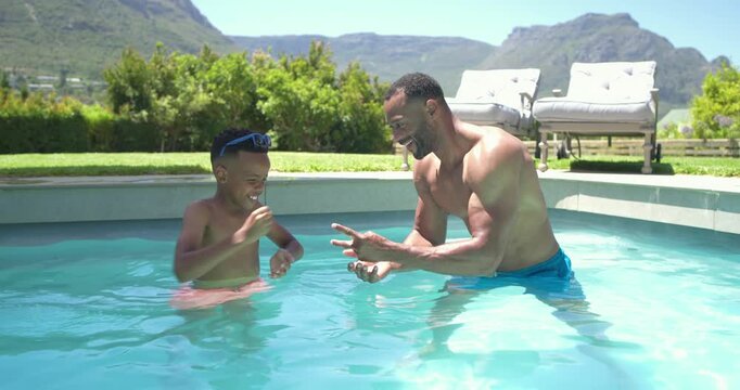 Father initiating game, reaching toward child with pink trunks blue goggles playing for fun in pool