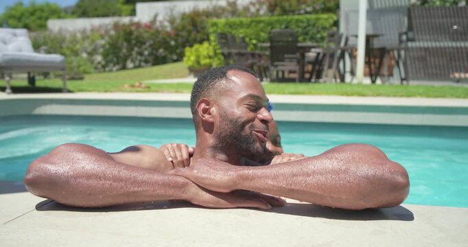 African American father and son in swimwear hugging at pool edge, child rising with blue sunglasses