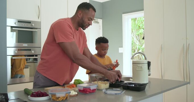 African American father and son in salmon mustard tees post-prep filling black meal trays at island