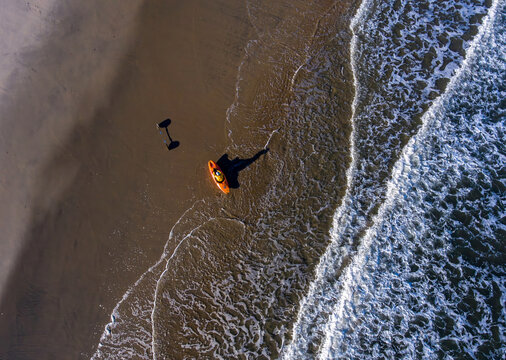 Aerial view of a vibrant orange kayak resting on the sandy shore as waves crash, casting long shadows on the beach, Atlantic City, New Jersey, United States.