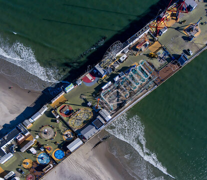 Aerial view of the Steel Pier amusement park extending into the ocean, a stark contrast of vibrant rides against the deep blues and greens of the water, Atlantic City, New Jersey, United States.