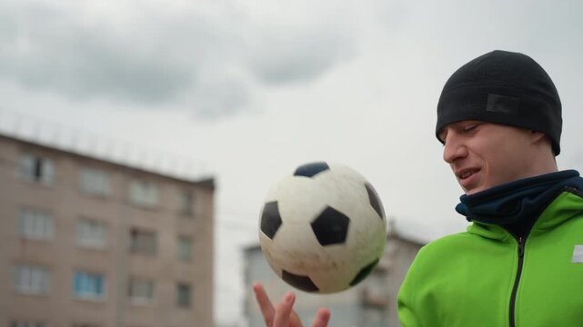 young player training in city yard, streetstyle athlete practicing with soccer ball under cloudy skies, individual in casual sportswear focusing on ball control outdoors on foggy day